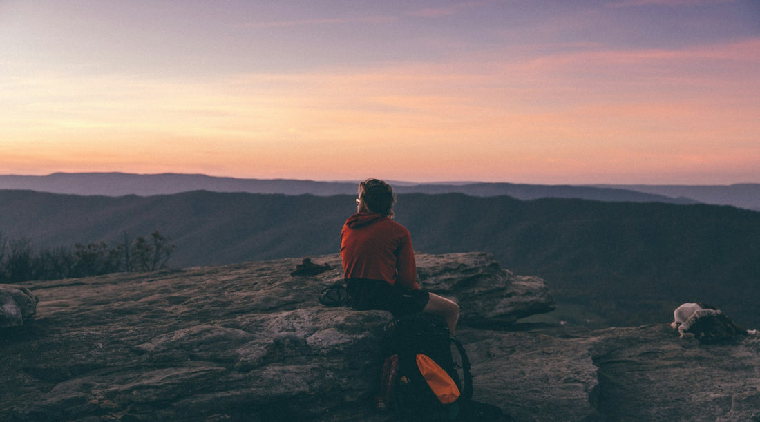 Person sitting on a boulder above a mountain valley at golden hour, a calm moment in a daily CBD spray routine