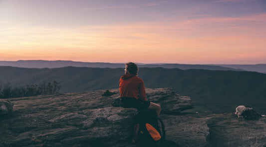 Person sitting on a boulder above a mountain valley at golden hour, a calm moment in a daily CBD spray routine