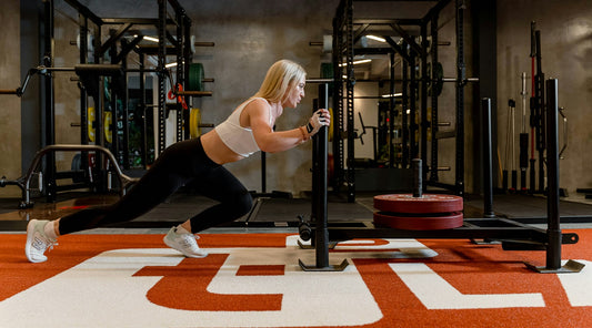 Woman pushing a weighted sled across a gym floor, part of a HYROX training block that needs a planned recovery routine