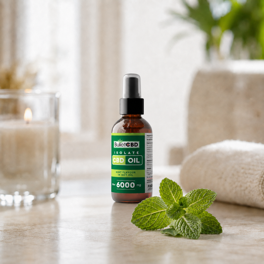 A bottle of Bullet CBD Isolate CBD Oil, 6000 mg, standing on a marble countertop with fresh mint leaves in front. The background is a softly blurred bathroom setting featuring a lit candle and a rolled towel.